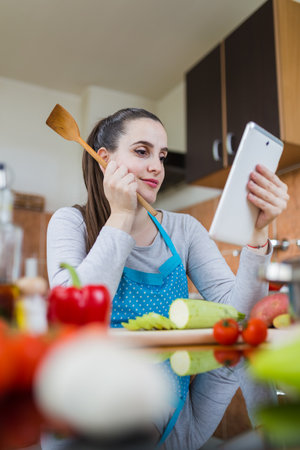 Woman using digital tablet in kitchen to find healthy meal recipe on the internet.の写真素材
