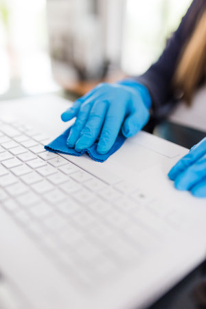 Close up of female hands in surgical protective gloves cleaning laptop keyboard with microfiber cloth.の写真素材