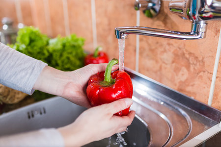 Housewife washing paprika in kitchen sink. Homemade food preparation concept.の写真素材