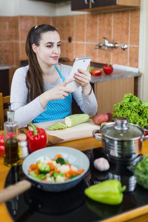 Young housewife learning to cook by watching online video recipe tutorial.の写真素材