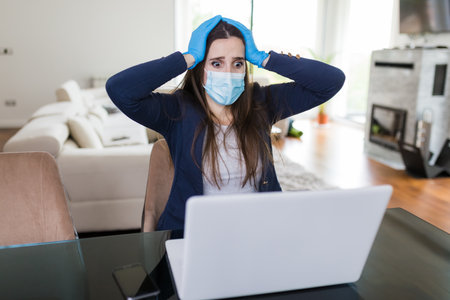 Young businesswoman with surgical mask and gloves working on laptop under stress. Coronavirus and business concept.の写真素材
