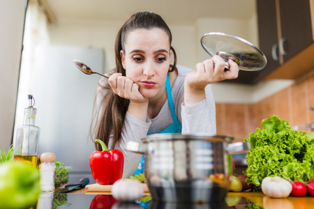 Unhappy woman looking at pot in kitchen. Food preparing failure concept.の写真素材