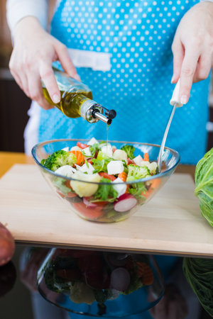Close up of woman in apron preparing vegetable salad and adding olive oil at home kitchen desk.の写真素材