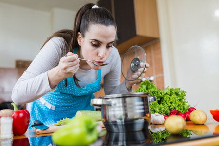 Housewife tasting food from pot with spoon. Healthy meal preparation.の写真素材