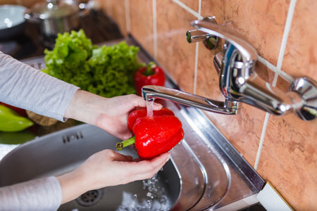 Close up of woman hands washing bell pepper in modern kitchen.の写真素材