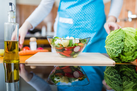 Bowl of vegetable salad on table with woman in apron in the background.の写真素材