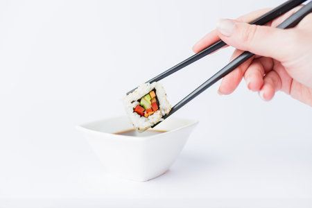 Close up of woman holding chopsticks with sushi roll and bowl with soy sauce on table, japanese traditional healthy meal concept.の写真素材