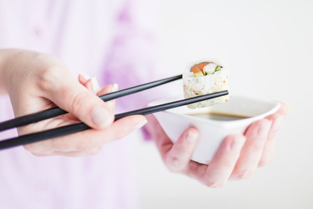 Close up of woman holding bowl with soy sauce and chopsticks with sushi roll, japanese traditional healthy meal concept.の写真素材