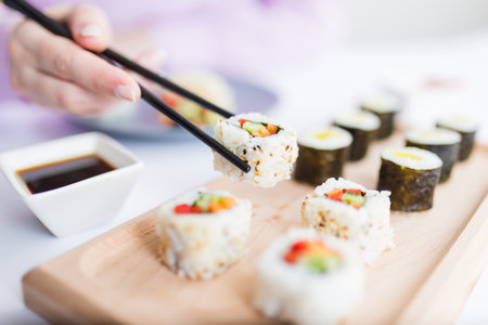 Close up of female eating sushi portion roll with chopsticks at restaurant.の写真素材