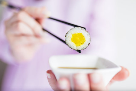 Female dipping tasty sushi maki or uramaki with chopsticks into bowl with soy sauce.の写真素材