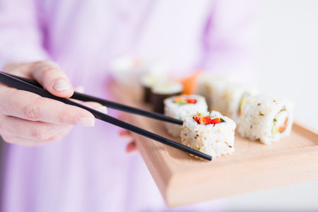 Close up of woman holding wooden platter sushi set and chopsticks.の写真素材