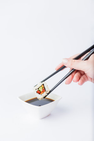 Close up of woman holding chopsticks with sushi roll and bowl with soy sauce on table, japanese traditional healthy meal concept.の写真素材