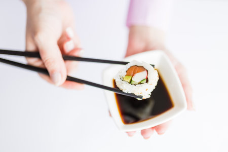 Close up of woman holding bowl with soy sauce and chopsticks with sushi roll, japanese traditional healthy meal concept.の写真素材