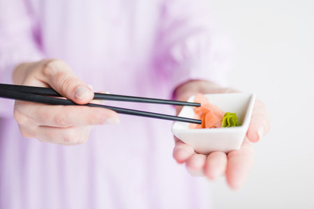 Close up of woman holding bowl with wasabi and gari and chopsticks with sushi roll, japanese traditional healthy meal concept.の写真素材