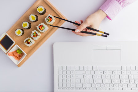 High angle view of businesswoman eating sushi next to her laptop. Take away japanese food and online order concept.の写真素材