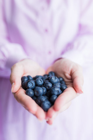 Healthy eating, vegetarian food and people concept - close up of young woman hands holding blueberriesの写真素材