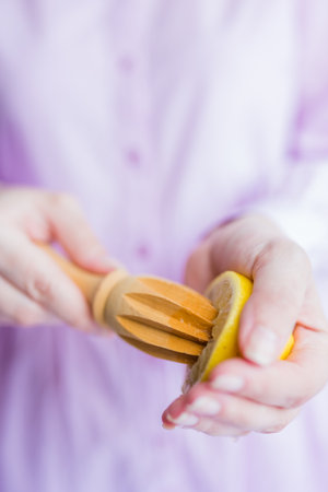 Female hands squeezing fresh lemon juice with wooden reamer, lemonade concept.の写真素材