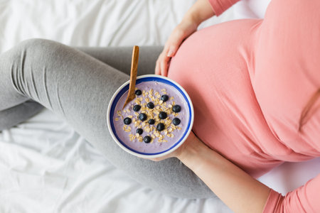 Female holding bowl with fresh muesli on bed. Pregnancy and healthy lifestyle concept.の写真素材