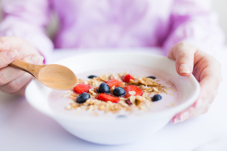 Close up of young female having healthy meal breakfast with cereals, strawberries and blueberriesの写真素材