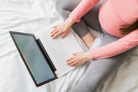 Above view of pregnant woman working on laptop while sitting on bed at home.の写真素材