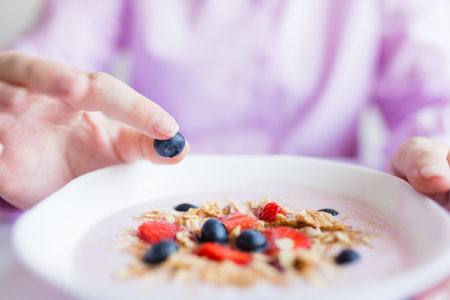 Close up of female hand adding one blueberry in plate with muesli, healthy meal concept.の写真素材