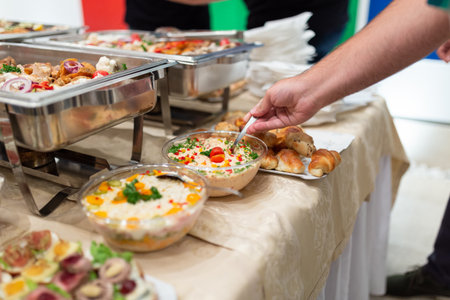 Close up of man hand serving himself a fresh salad from buffet catering table at restaurant or hotelの写真素材