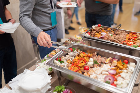 Close up of man holding plate and scooping food at buffet table catering in hotel or restaurantの写真素材