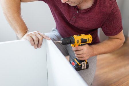 Close up of man holding electrical battery screwdriver while installing wooden kitchen shelvesの写真素材