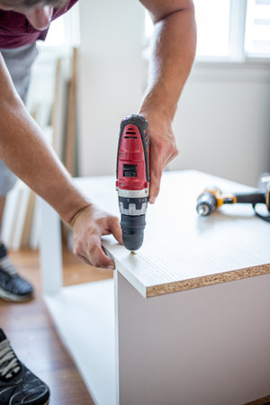 Man installing wooden shelves by using cordless screwdriverの写真素材