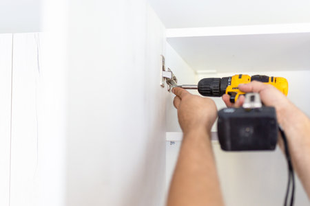 Handyman using screwdriver while installing kitchen cabinets at homeの写真素材