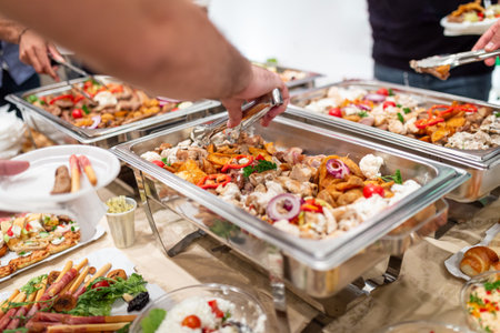 Close up of man hand scooping food with tongs from chafing dish from buffet table on celebration event party.の写真素材