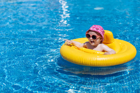 Cute little girl in swimming pool with swimming float, wearing sunglasses and colorful hat. Children and summer season concept.の写真素材