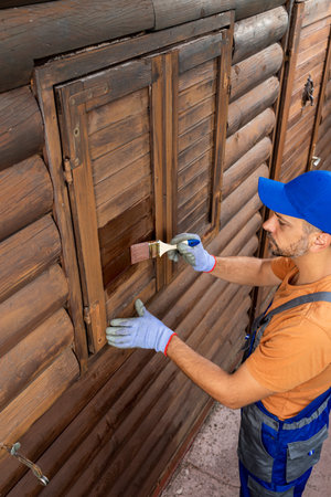 Worker in protective clothing staining wooden window shutters on house external walls.の写真素材