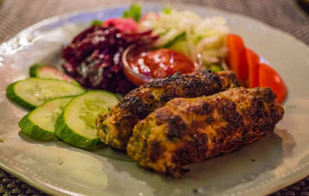 A traditional dish of kebab on a plate, cooked on a grill, along with vegetables.の写真素材