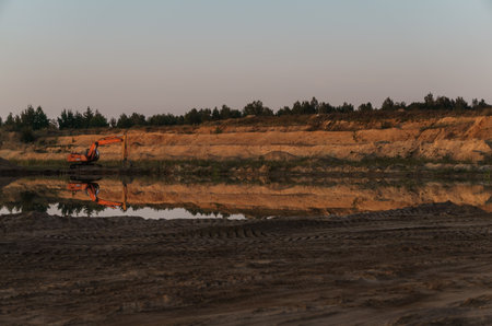 Excavator on the shore of a sand pit turning into a pondのeditorial素材