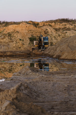 Excavator on the shore of a sand pit turning into a pondのeditorial素材
