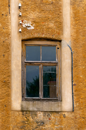 An old window in a wooden frame in the opening of an old house
