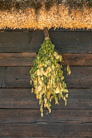 A birch broom for a bath hangs on the wall under the roof.の写真素材