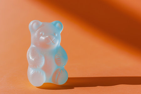 Blue gummy bear on a orange background with a shadowの素材