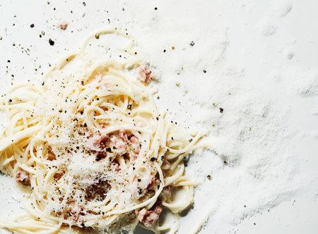 Spaghetti carbonara with ham and parmesan splattered across table on white backgroundの素材