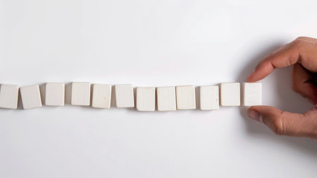 hand arranging a row of white wooden blocks on a white background.の素材