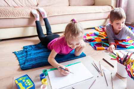 Boy and girl paint and felt-tip pens at home during a pandemic to Vivaldi's music - Summer. Children draw with paints and pencilsの写真素材