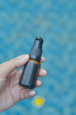 a hand holding a lotion packaging bottle display with a close-up angle with a clear swimming pool water backgroundの写真素材