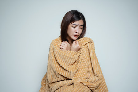 a woman who is sick with cold and flu uses a thick blanket to warm herselfの写真素材