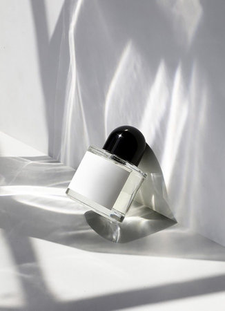 Minimalist perfume bottle with black cap placed on a white surface with artistic light reflections...