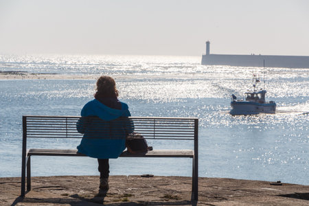 Woman sitting on a bench and waiting for the fishing boat returning to Poulgoazec harbor