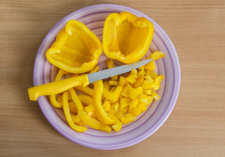 Half and pieces of yellow pepper on a plate with e knifeの写真素材