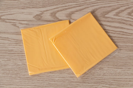 Two portions of processed cheese with cheddar in plastic packaging