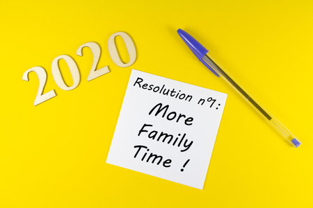 Pen, paper with resolution more family time and 2020 in wooden figures on yellow backgroundの写真素材
