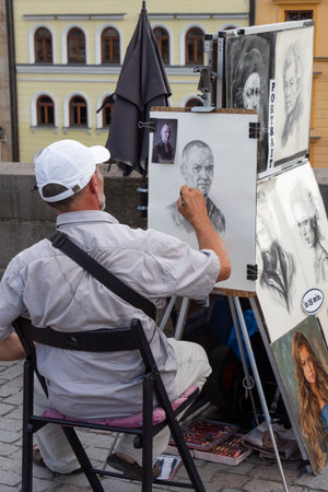 PRAGUE - CZECH REPUBLIC, AUGUST 13, 2019 : portrait painter drawing a face from a picture in a streetのeditorial素材